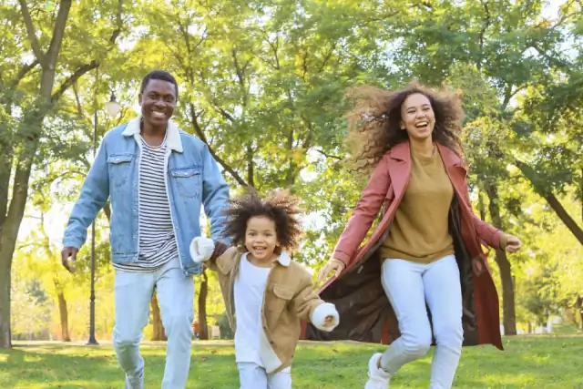 Une famille, père, mère et fille, court en riant dans un parc